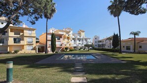 Um conjunto de edifícios residenciais com várias varandas, um pátio central com piscina e áreas verdes ao redor.