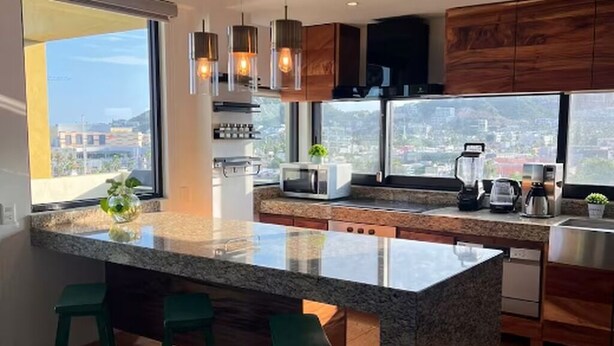 Cozinha moderna com uma ilha grande, banquetas, vista para a cidade e armários de madeira.