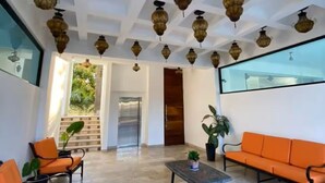 Um hall espaçoso com teto alto, pisos de azulejos estampados e um espaço de estar com sofás e poltronas laranja.