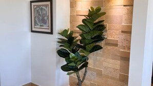 Uma planta em vaso num corredor com chão de azulejos e parede de pedra.
