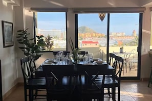 Ein Essbereich mit Tisch für vier Personen, großen Fenstern und Blick auf die Stadt sowie einem Blumentopf.
