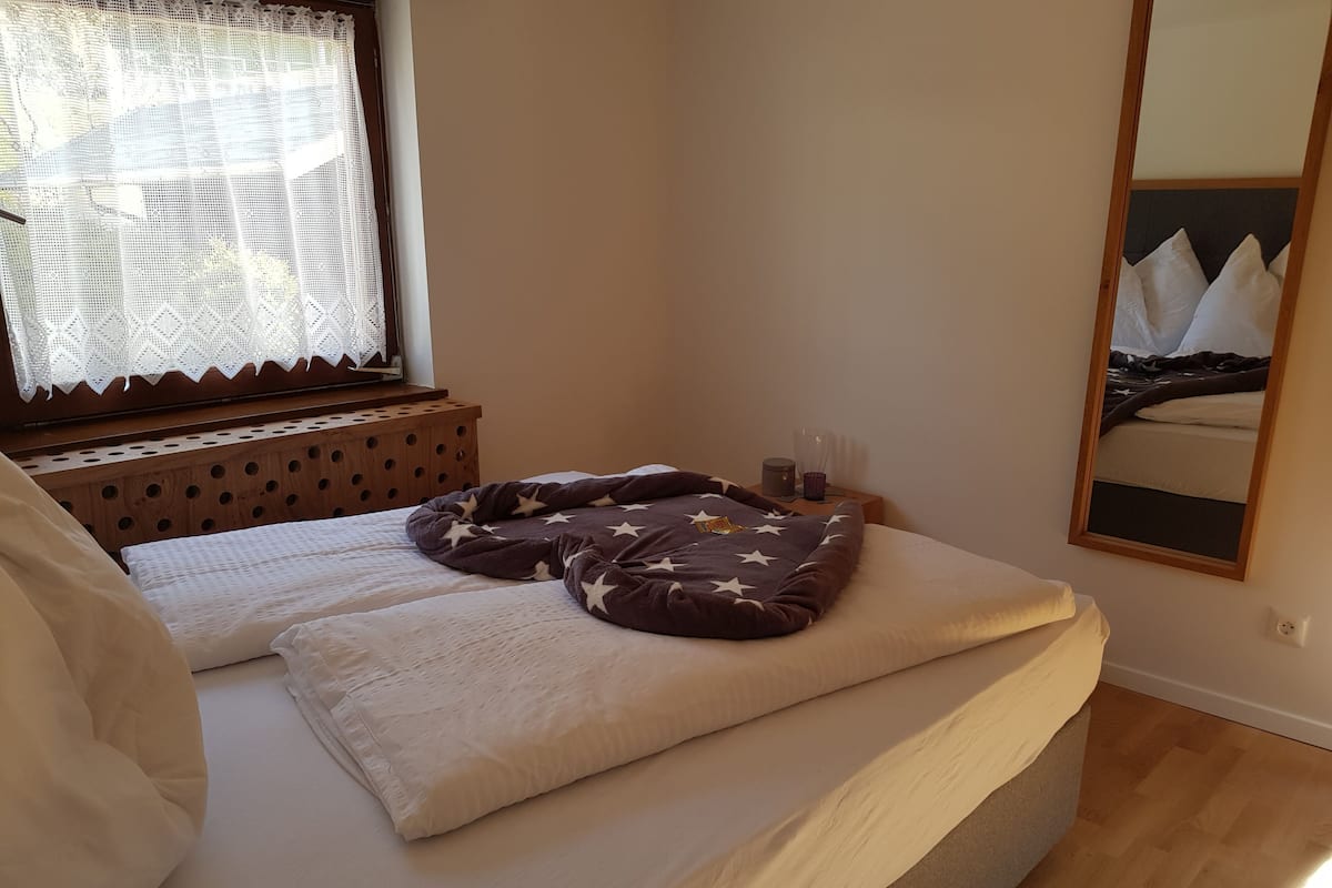 A neatly made bed with a star-patterned blanket, a wooden nightstand with a lamp, and a mirror on the wall.