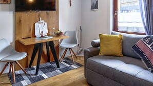 Un saló modern amb un sofà gris, una taula de dinar de fusta i una televisió penjada a la paret.