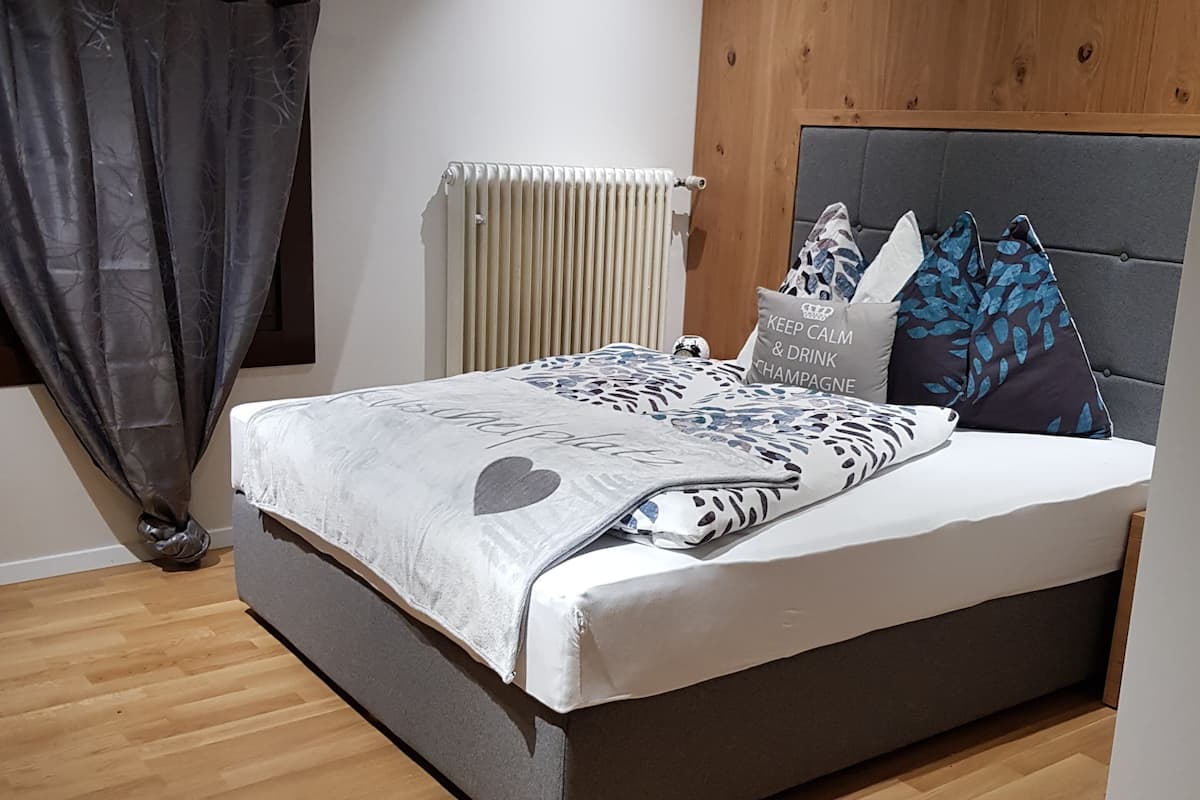 A bedroom with a bed, wooden floor, radiator, and a window with curtains.