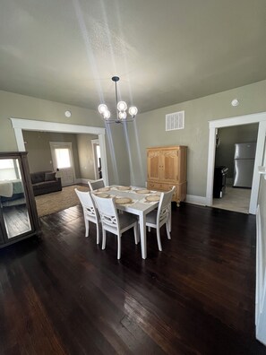 A dining area with a white table and chairs, a wooden cabinet, and a kitchen in the background. - 2-bedroom house in tranquil Great Bend with AC comfort (Great Bend)