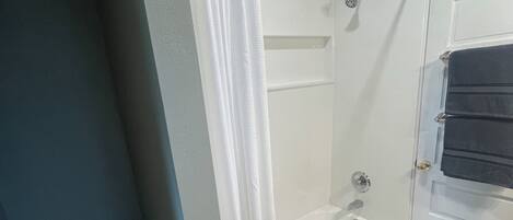 A bathroom with a toilet, bathtub, shower, and a door with a towel rack.