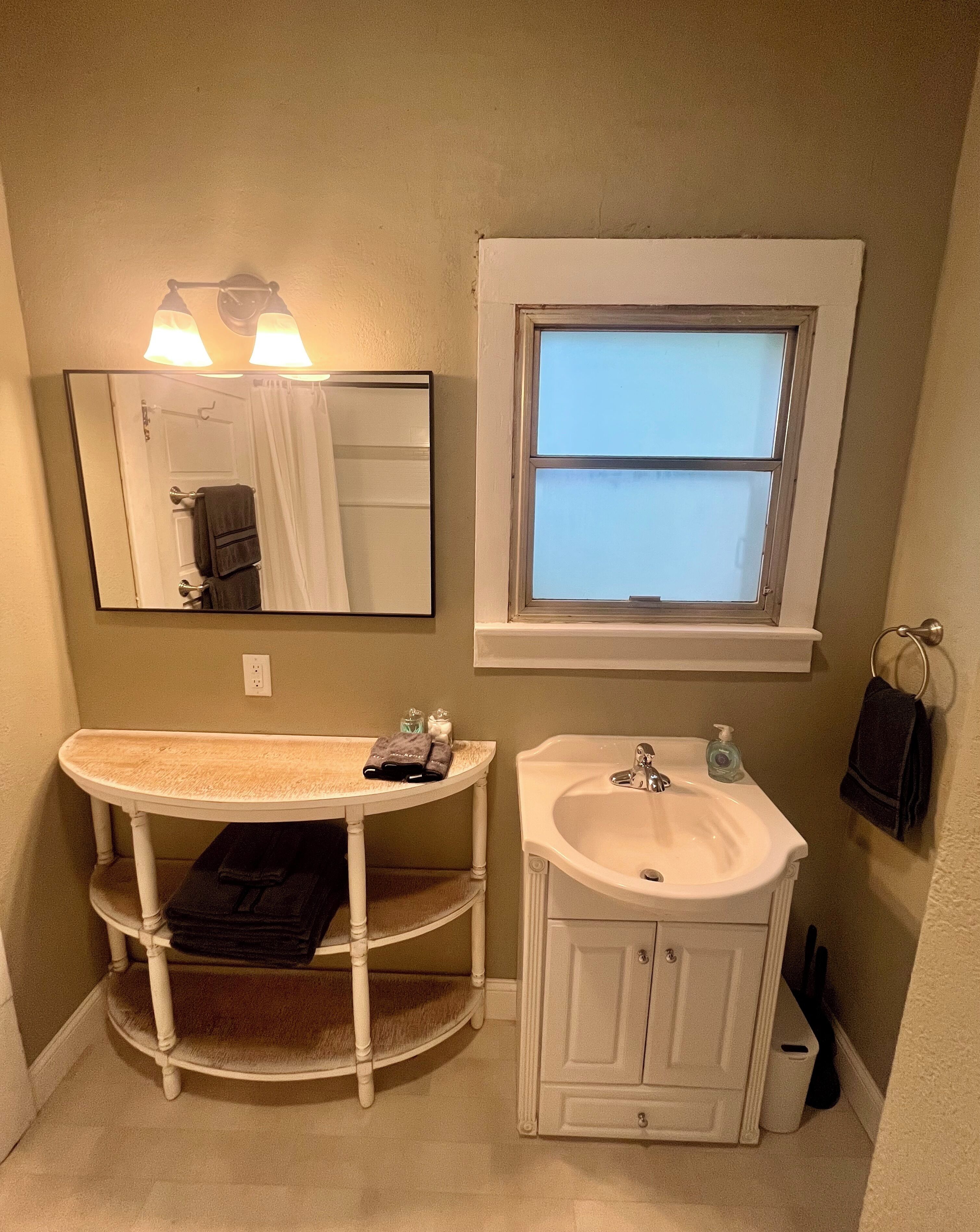 A bathroom with a vanity, two sinks, a window, and a mirror.