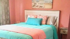 Una cama con cabecera, una mesita de noche, un cuadro de una escena de playa y piso de madera.