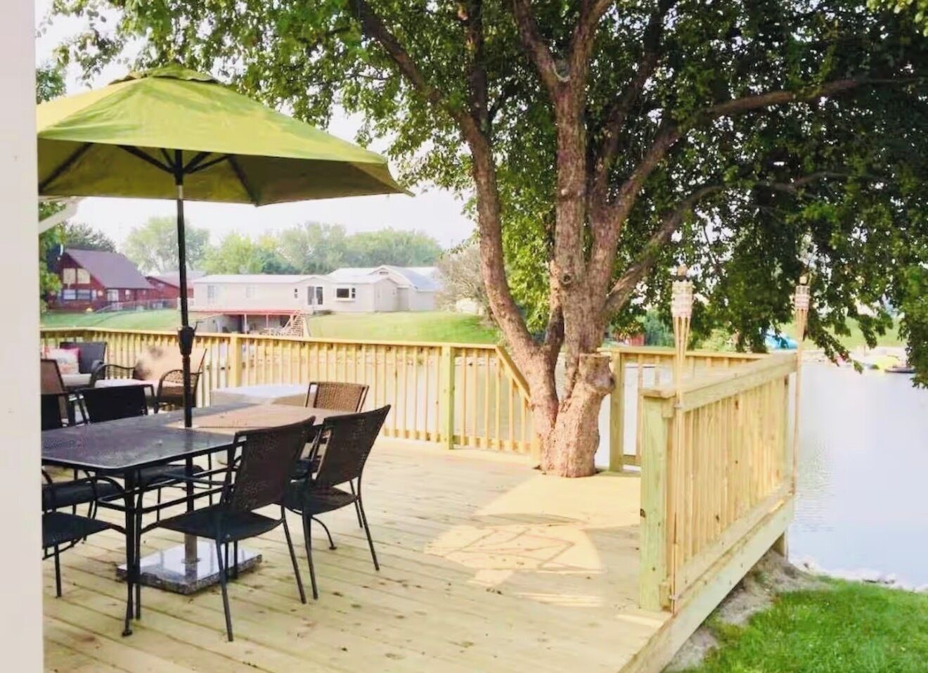 A wooden deck with a table and chairs, a green umbrella, and a tree.