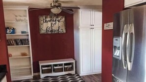 Una cocina con un refrigerador de acero inoxidable, un ventilador de techo, un armario blanco y una alfombra estampada.