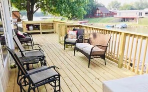 A wooden deck with outdoor furniture, including chairs and a sofa, overlooking a body of water with boats. - Lakefront Home-Sleeps 10, Private Dock, Kayaks, Family Friendly (Elwood)