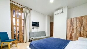 A bedroom with a bed, a television mounted on the wall, a chair, and a wooden door. - Hotel Granada Embassy (Cali)