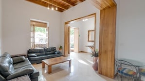 A spacious living room with a wooden ceiling, a black leather sofa, a wooden coffee table, and a glass table with metal chairs. - Hotel Granada Embassy (Cali)