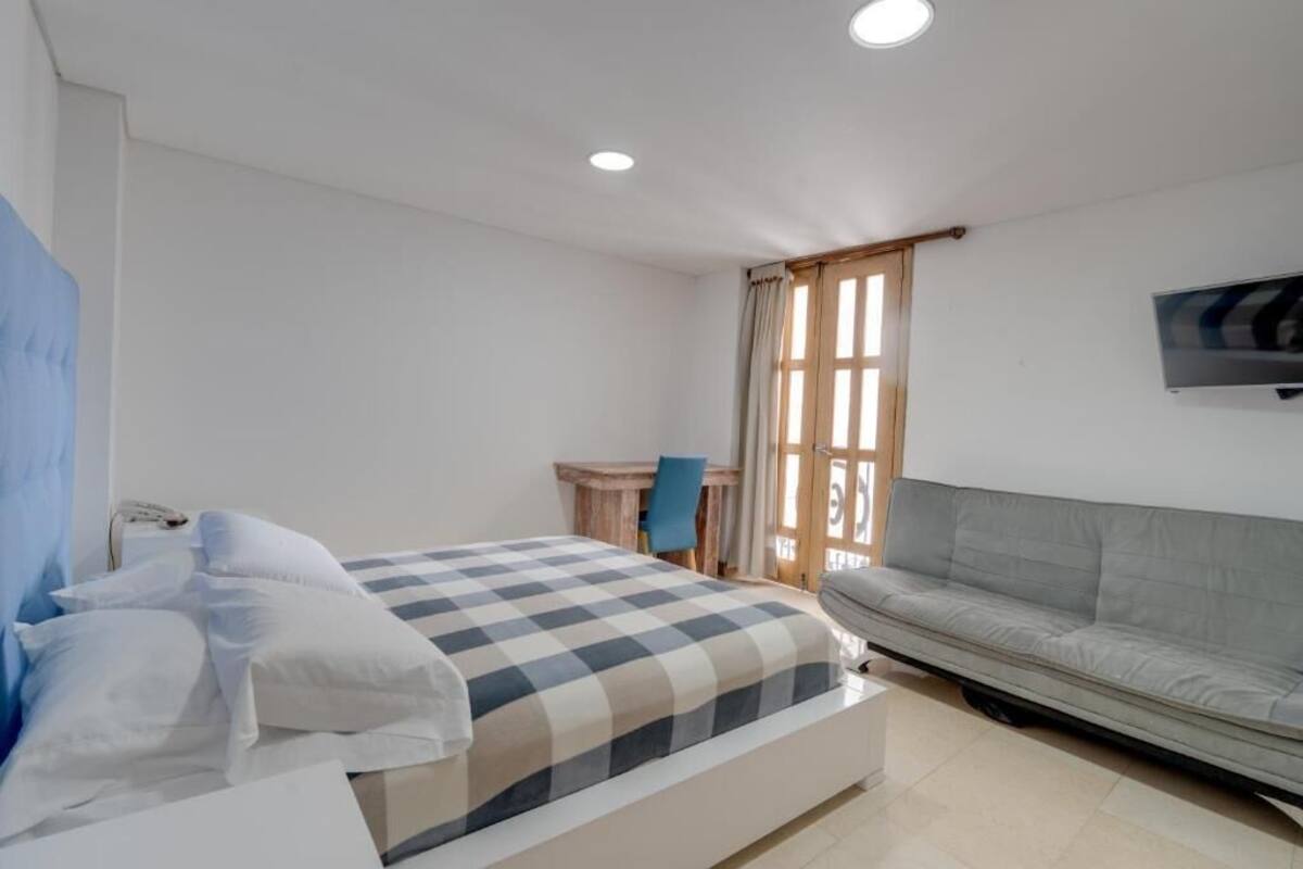 Un dormitorio con cama, escritorio, silla, sofá y televisor en la pared.