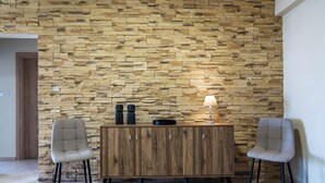 Ein Zimmer mit Steinwand, Holzschrank, zwei Stühlen und einem Tisch mit Lampe.