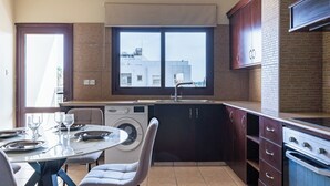 Eine kompakte Küche mit Waschmaschine, eine Essecke mit Tisch für vier Personen und ein großes Fenster mit Blick auf eine Stadtlandschaft.