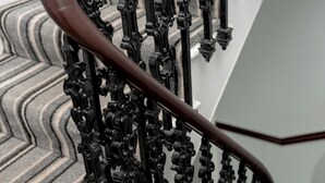 Eine Treppe mit aufwendiger schwarzer Metallgeländerung und einem Holnlauf.