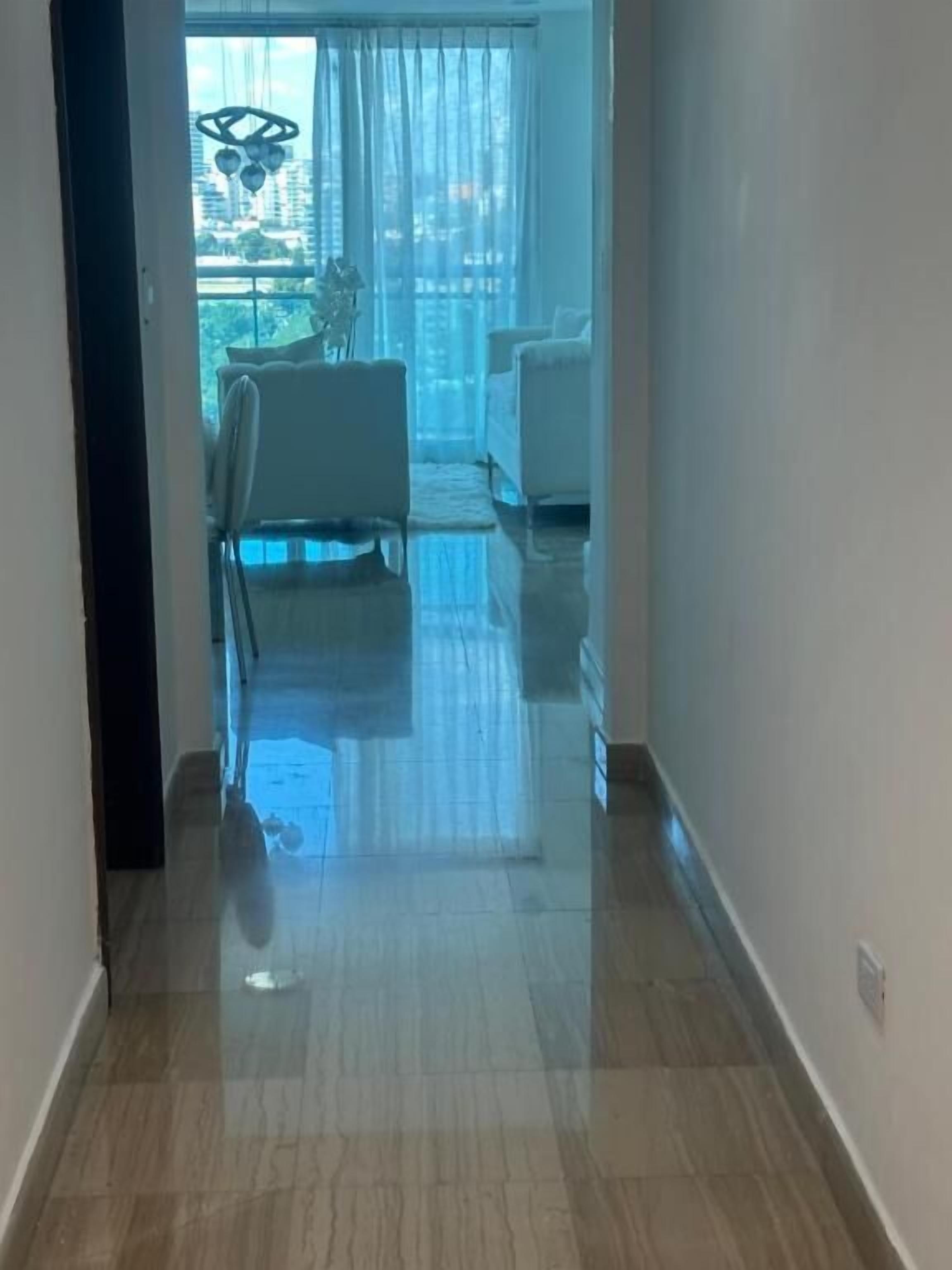 Un couloir au sol carrelé et brillant mène à une pièce où se trouve un canapé blanc et un coin repas avec une table et des chaises.