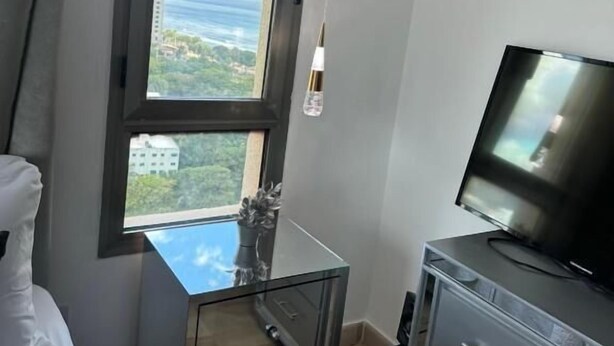 A bedroom with a large window, a bed, a TV, and a small cabinet. - Apartamento con Vista mar y la Ciudad La Gloria Malecón Santo Domingo (Santo Domingo)