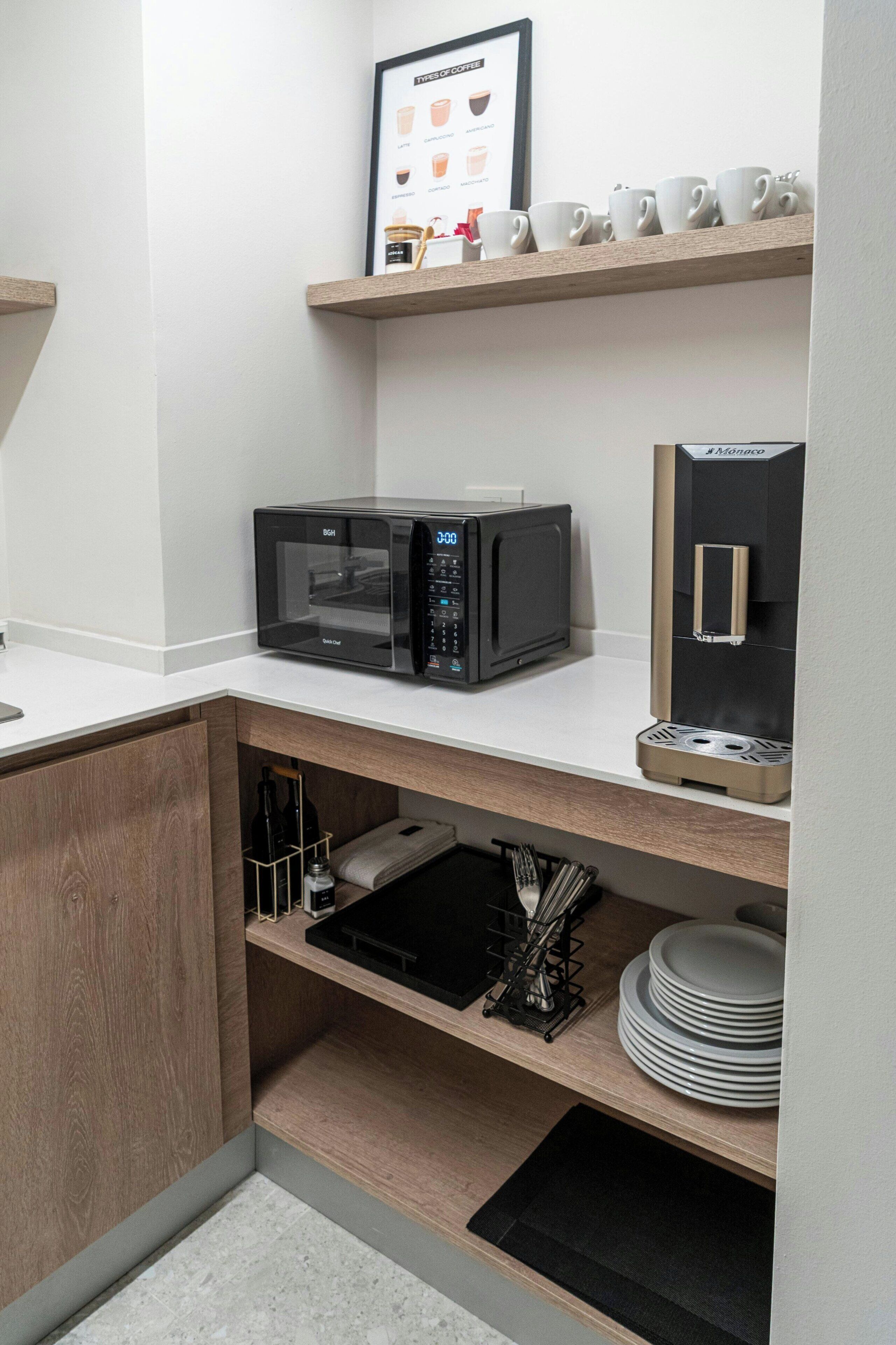 A kitchen with a microwave, coffee maker, and shelves with cups and plates.