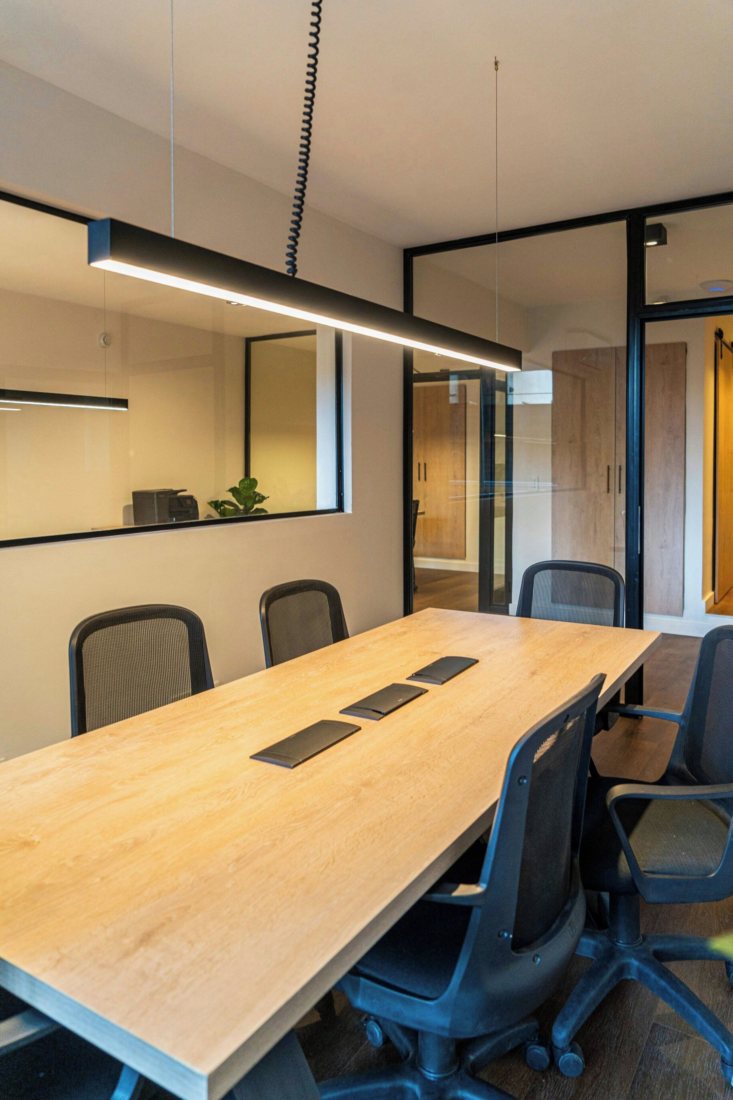A conference room with a long table, four chairs, and a modern pendant light.