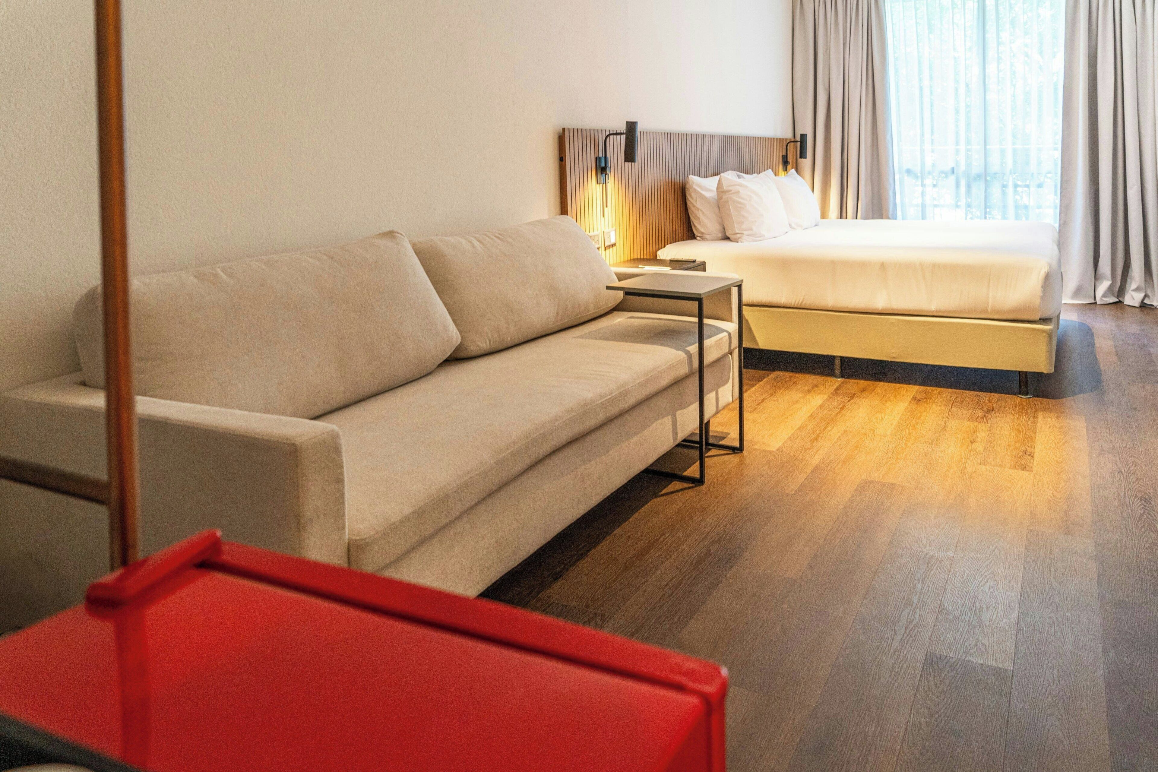 Une chambre d’hôtel avec un canapé, un lit, une petite table et une vue sur l’extérieur.