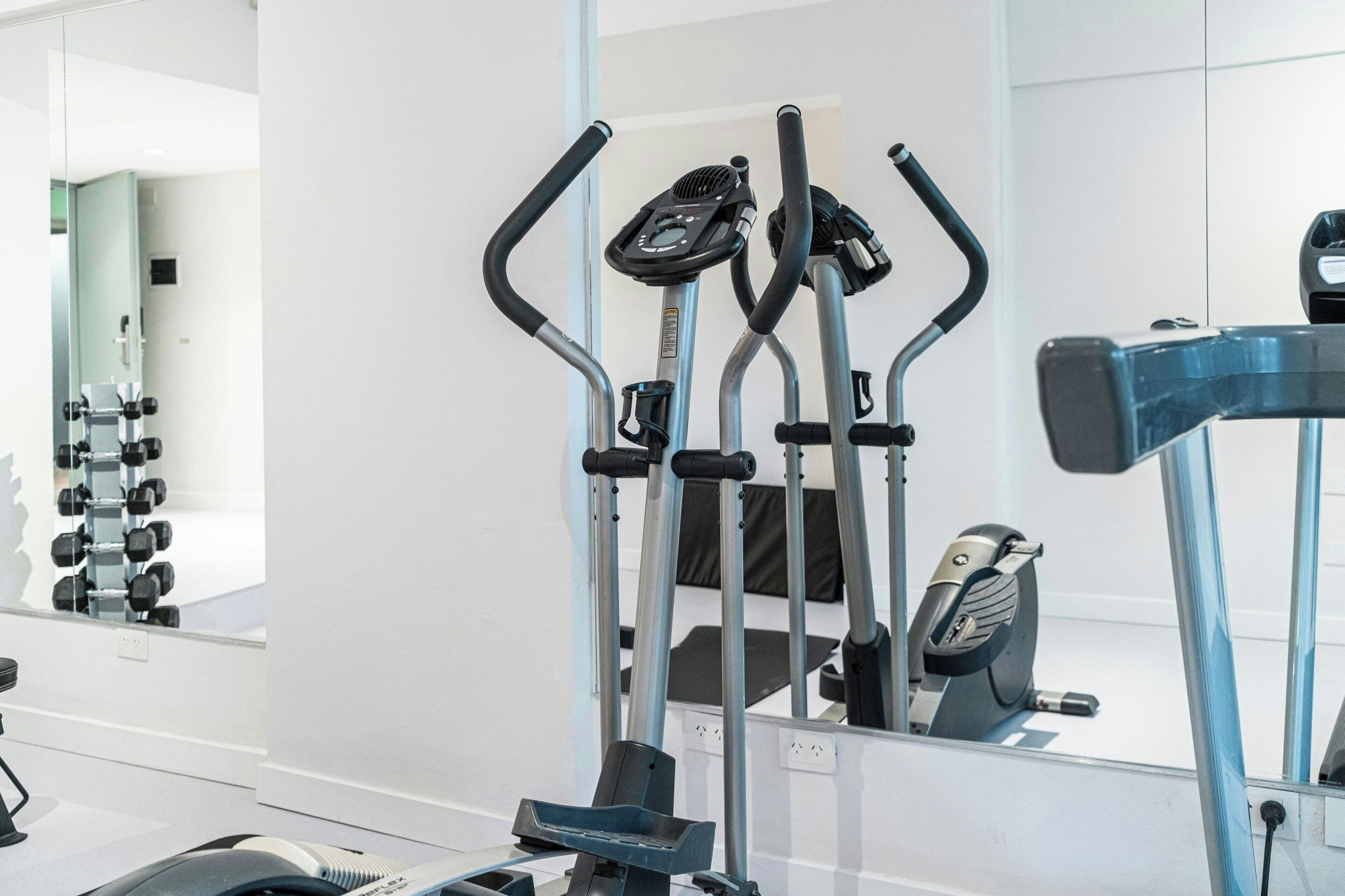 A gym with exercise equipment, a mirror, and a wall-mounted dumbbell rack.