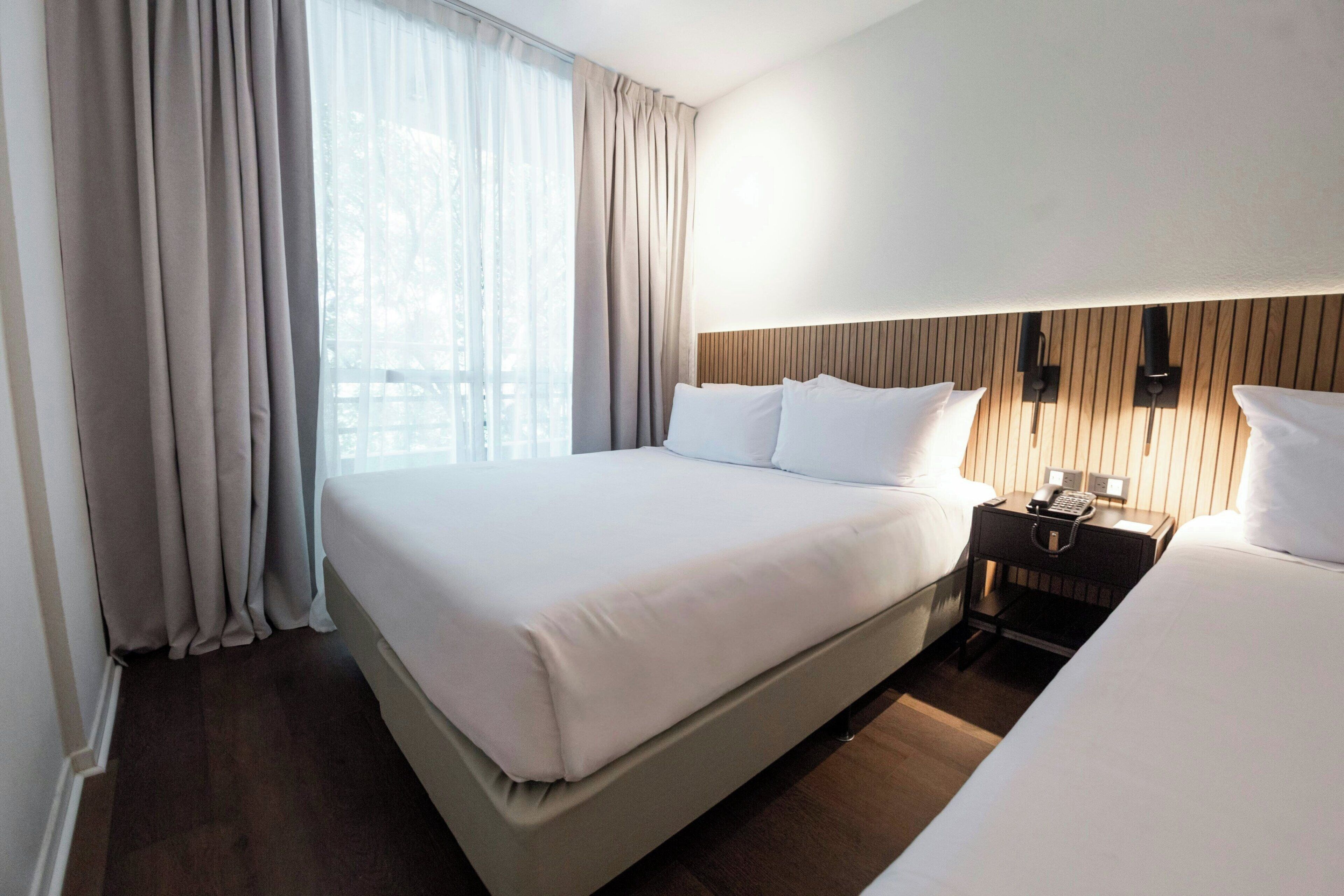 Ein Hotelzimmer mit einem großen Bett, einem Nachttisch mit Telefon und einem Fenster mit Vorhängen.