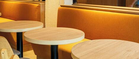 A hotel interior with round tables and wooden chairs, a reception desk with 'CITY EXPRESS PLUS BY HARRIOTT' signage, and a modern design.