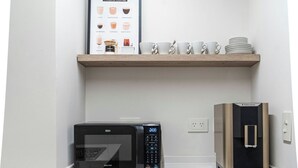 Ett kompakt kök med mikrovågsugn, kaffebryggare och en inramad affisch med information om olika kaffesorter på väggen.