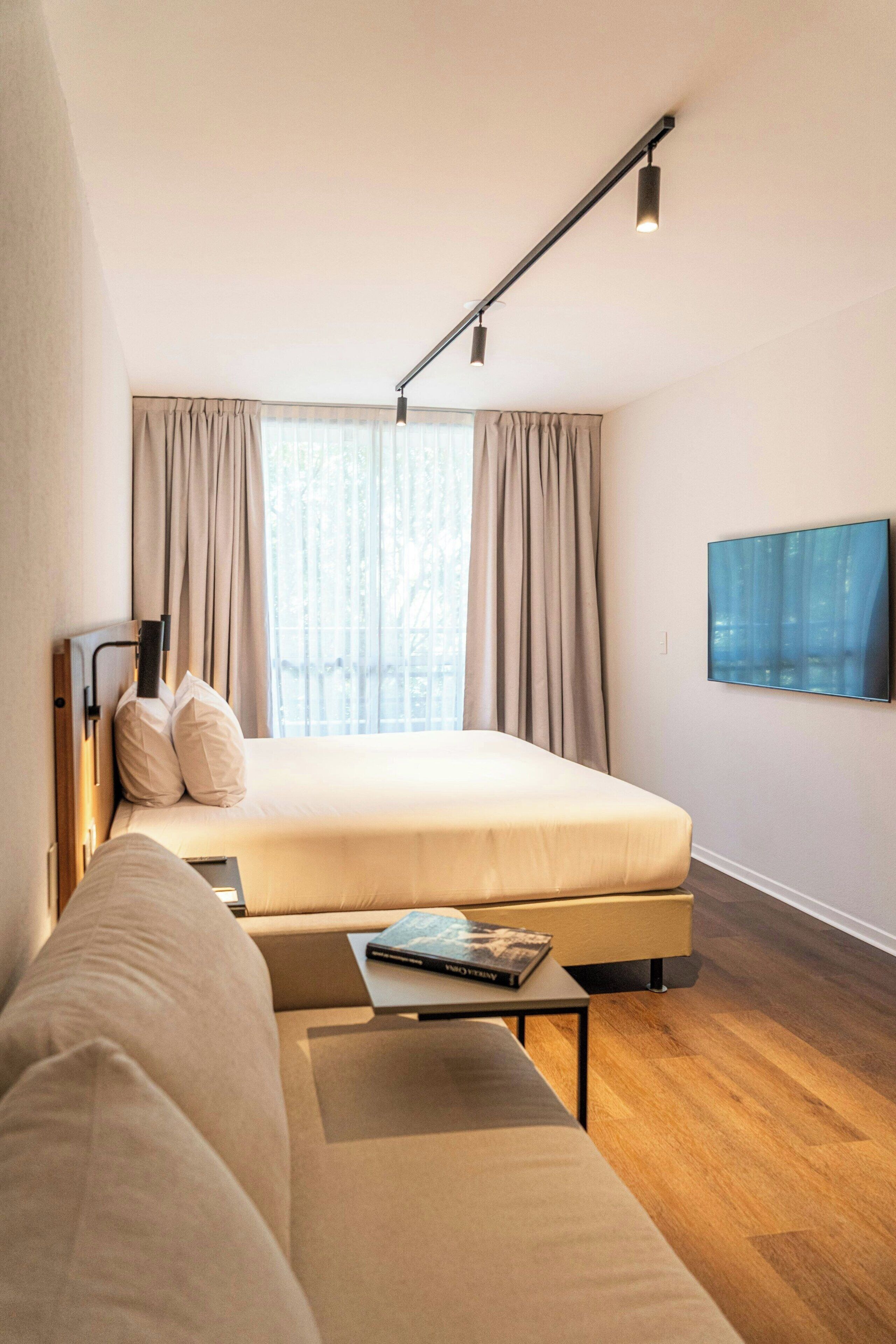 Una moderna camera d'albergo con un letto, una poltrona, una televisione a schermo piatto e una finestra con tende.