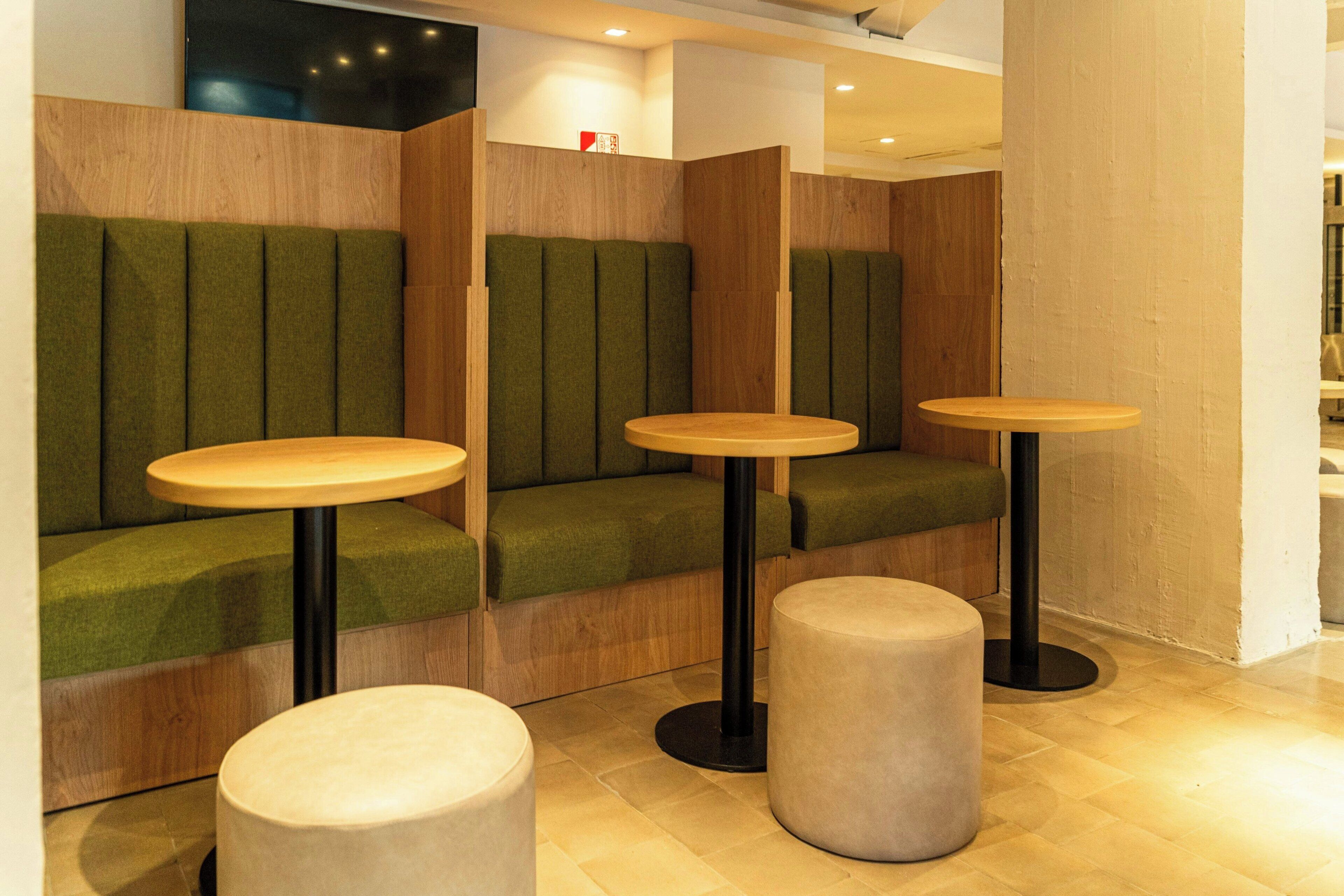 A seating area with cushioned booths and round tables, wooden accents, and a tiled floor.