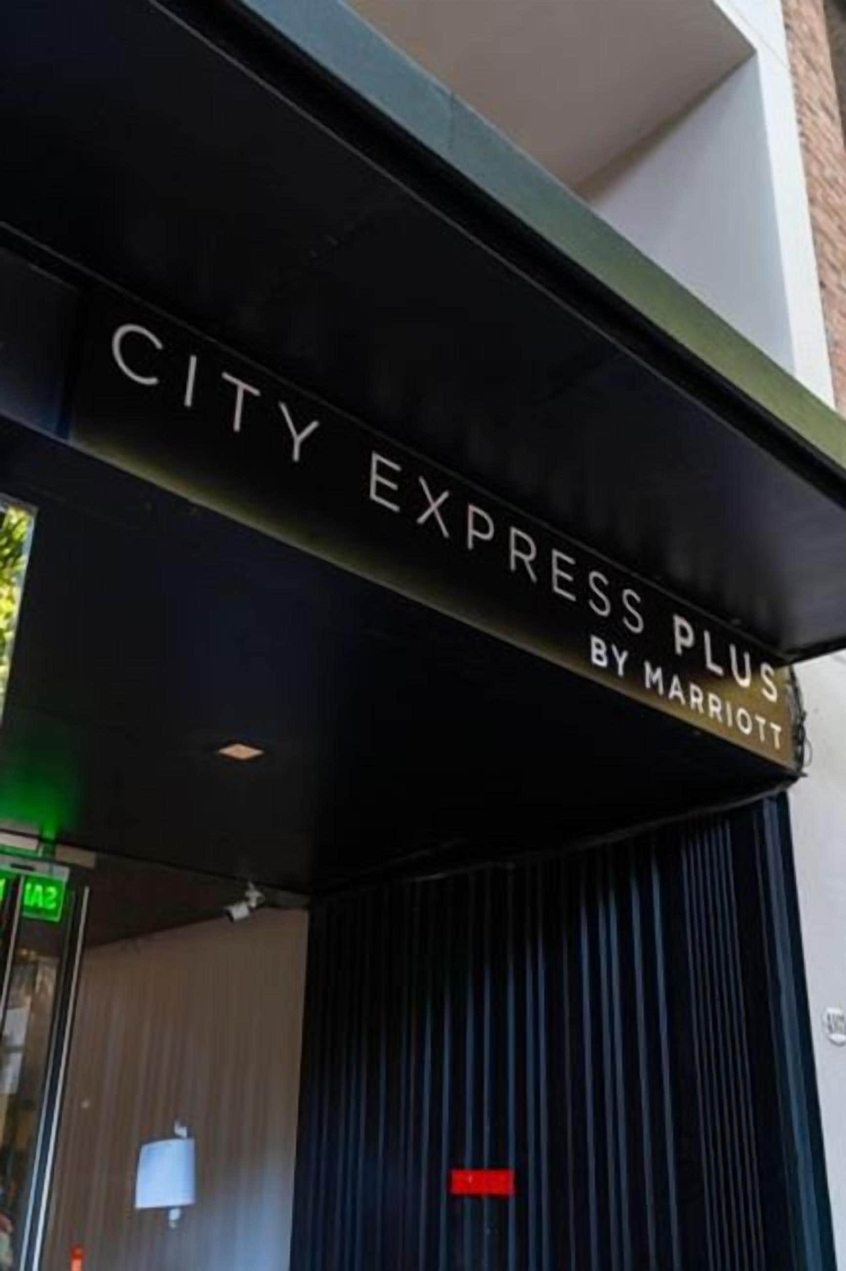 Ein Hotel Eingang mit einem Schild, auf dem 'CITY EXPRESS PLUS BY MARRIOTT' steht.