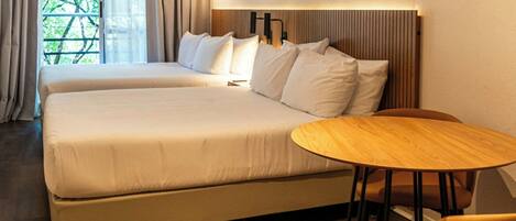 Habitación de hotel moderna con una cama grande, una mesa redonda de madera y vistas al exterior con vegetación.