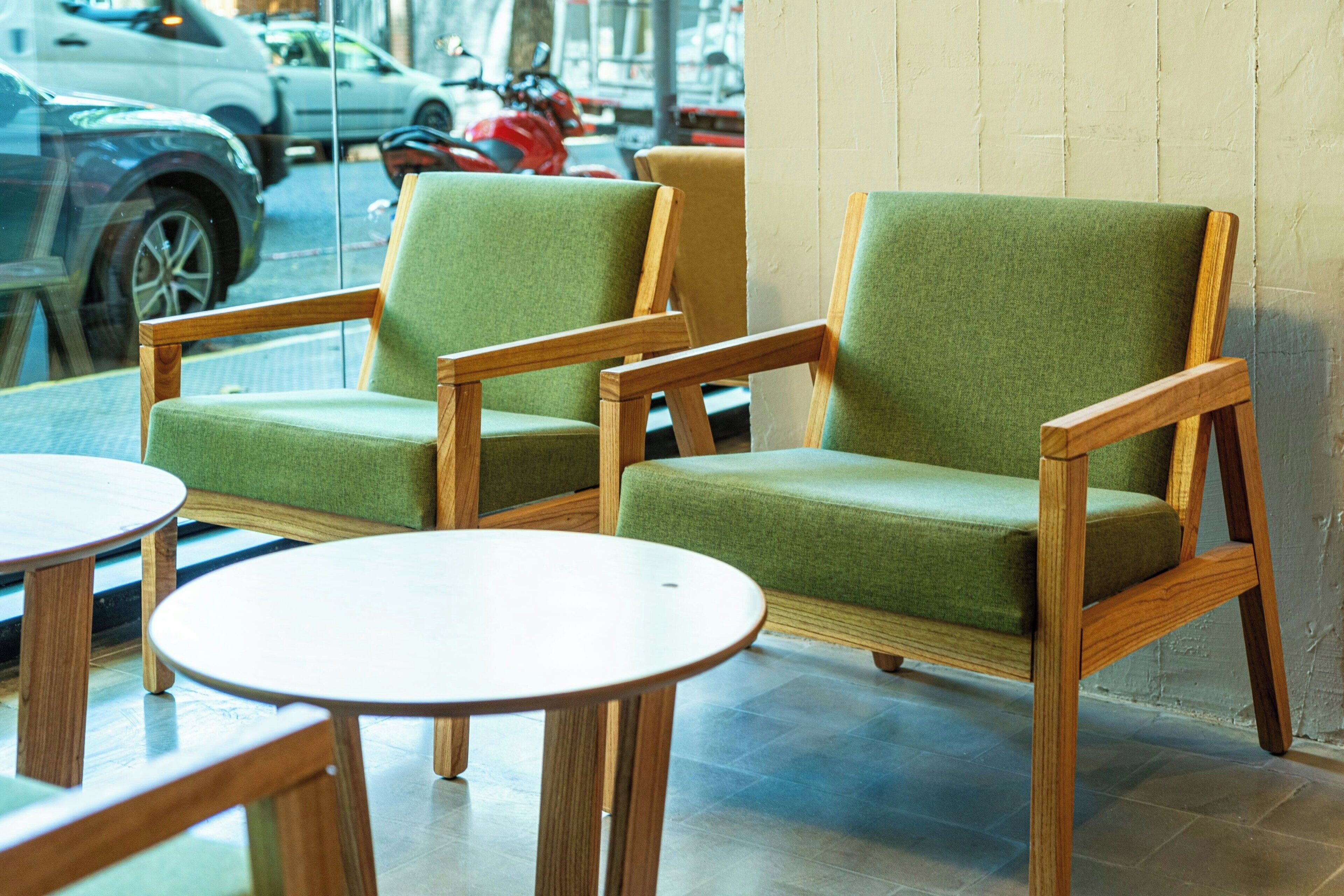 A seating area with two green upholstered chairs and two round wooden tables.