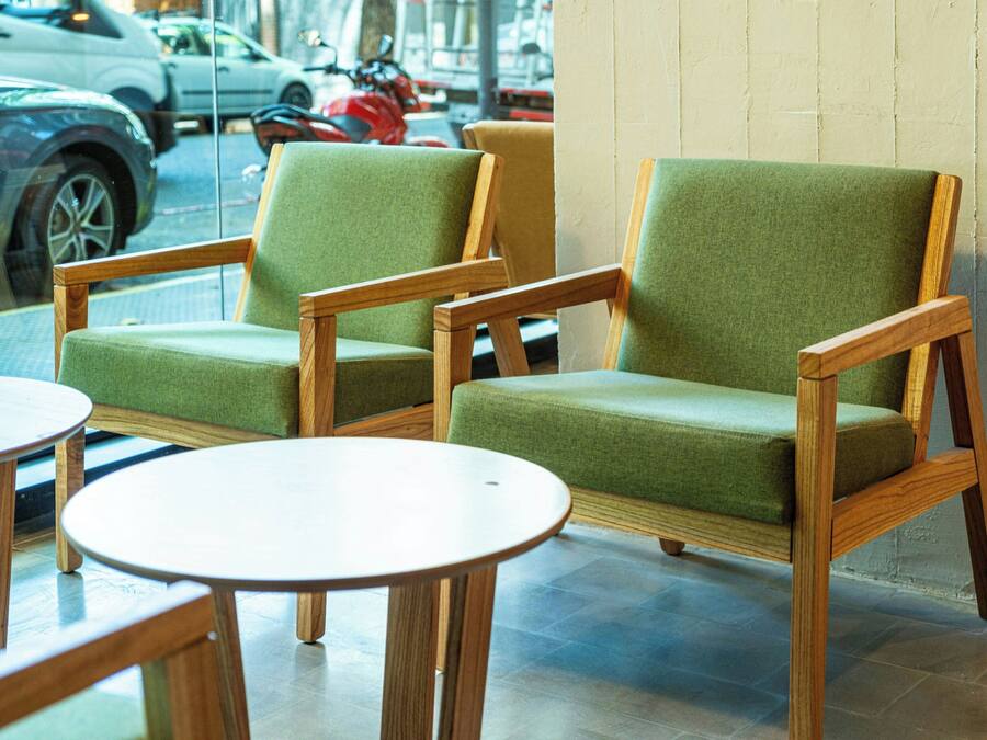 A seating area with two green upholstered chairs and two round wooden tables.