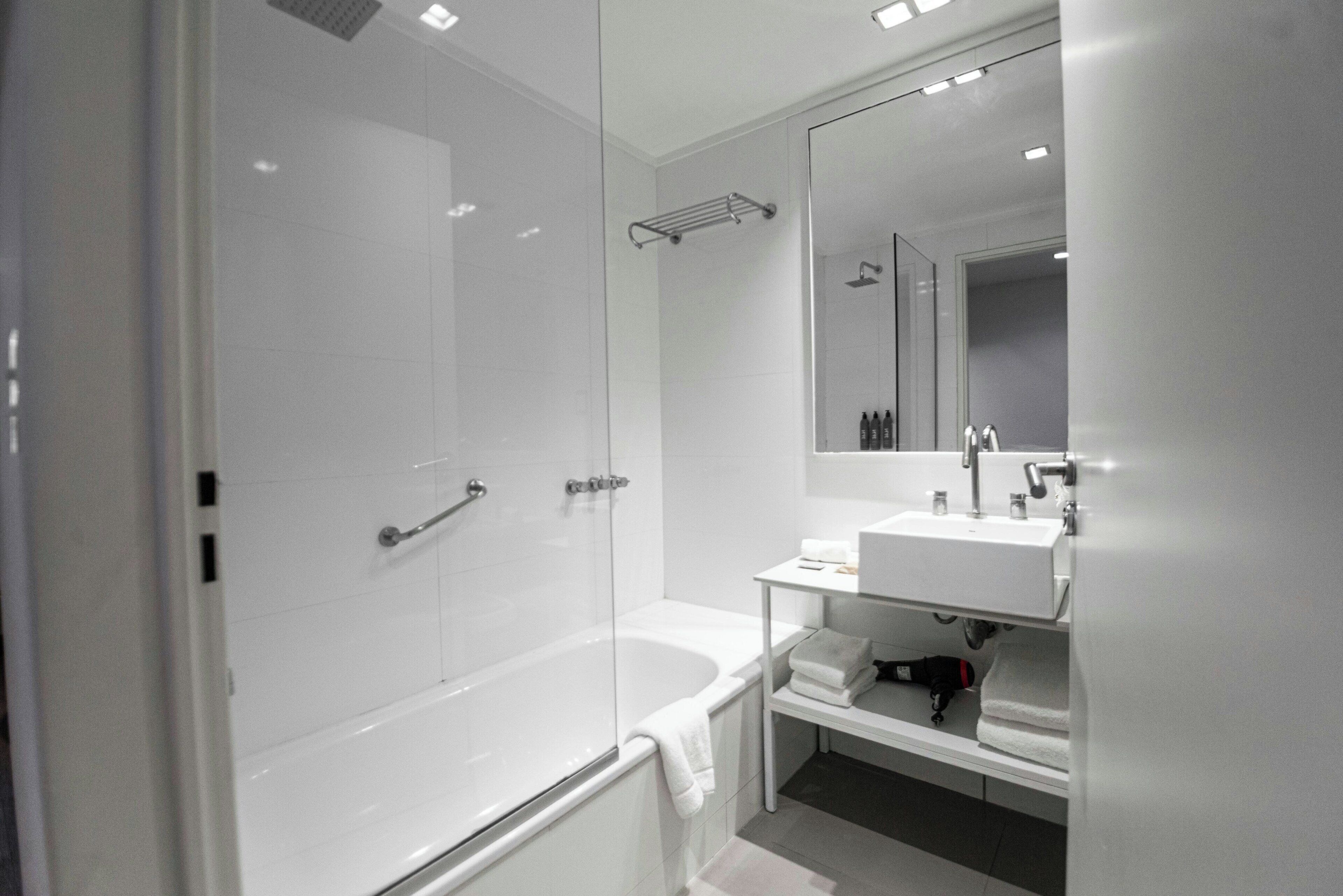 Un baño moderno con ducha envuelta en vidrio, una bañera blanca y un tocador con espejo.