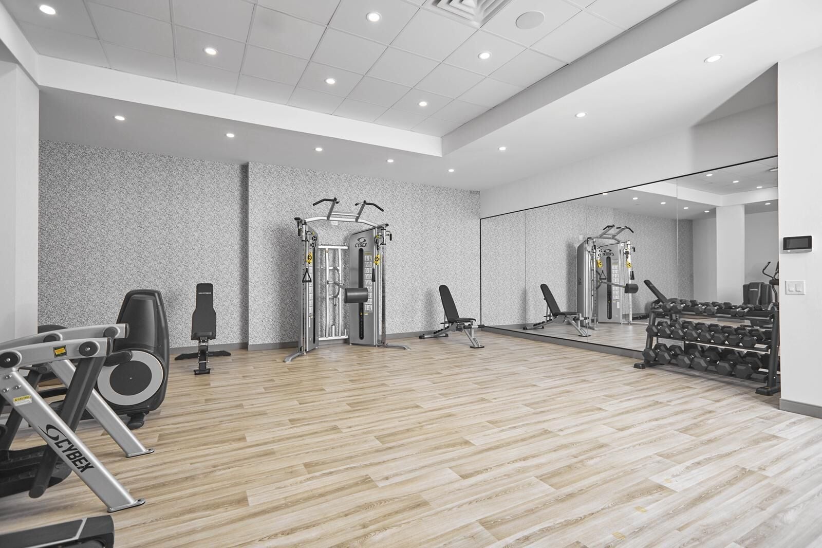 A modern gym with exercise equipment, a wooden floor, and a large mirror.