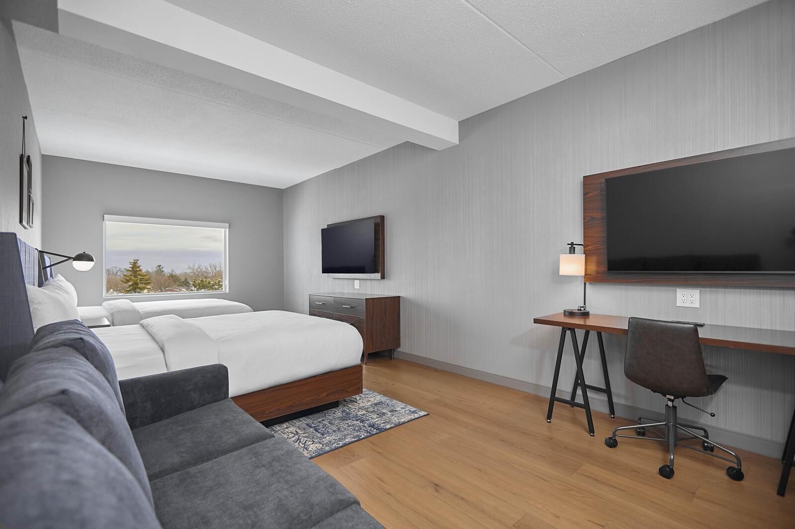Une chambre d’hôtel moderne équipée d’un lit, d’un bureau avec une chaise, d’une télévision et d’une grande fenêtre.