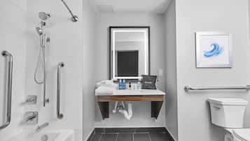 A modern bathroom with a shower, toilet, sink, and a framed artwork on the wall.