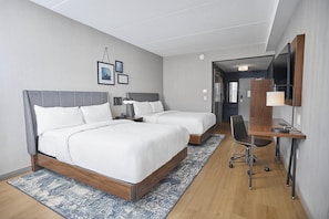 Une chambre d’hôtel avec deux lits, un bureau avec une chaise, une lampe de bureau, un miroir et un petit tapis.
