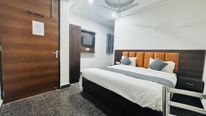 A hotel room with a bed, a TV, a ceiling fan, and a wooden door. - Vaayu Homestay (New Delhi)