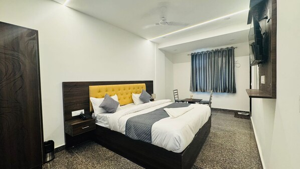 A modern hotel room with a large bed, a bedside table, a chair, a desk, and a window with curtains. - Vaayu Homestay (New Delhi)
