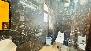 A bathroom with black marble walls, a white sink, a toilet, and a shower. - Vaayu Homestay (New Delhi)