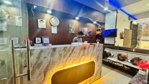 A reception desk with a marble top, a clock, framed pictures, and a digital screen. - Vaayu Homestay (New Delhi)