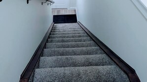 A staircase with a dark wooden handrail, carpeted steps, and a white door at the top. - 2 Bedroom Guest Suite in SW (Calgary)