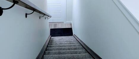 A staircase with a dark wooden handrail, carpeted steps, and a white door at the top.