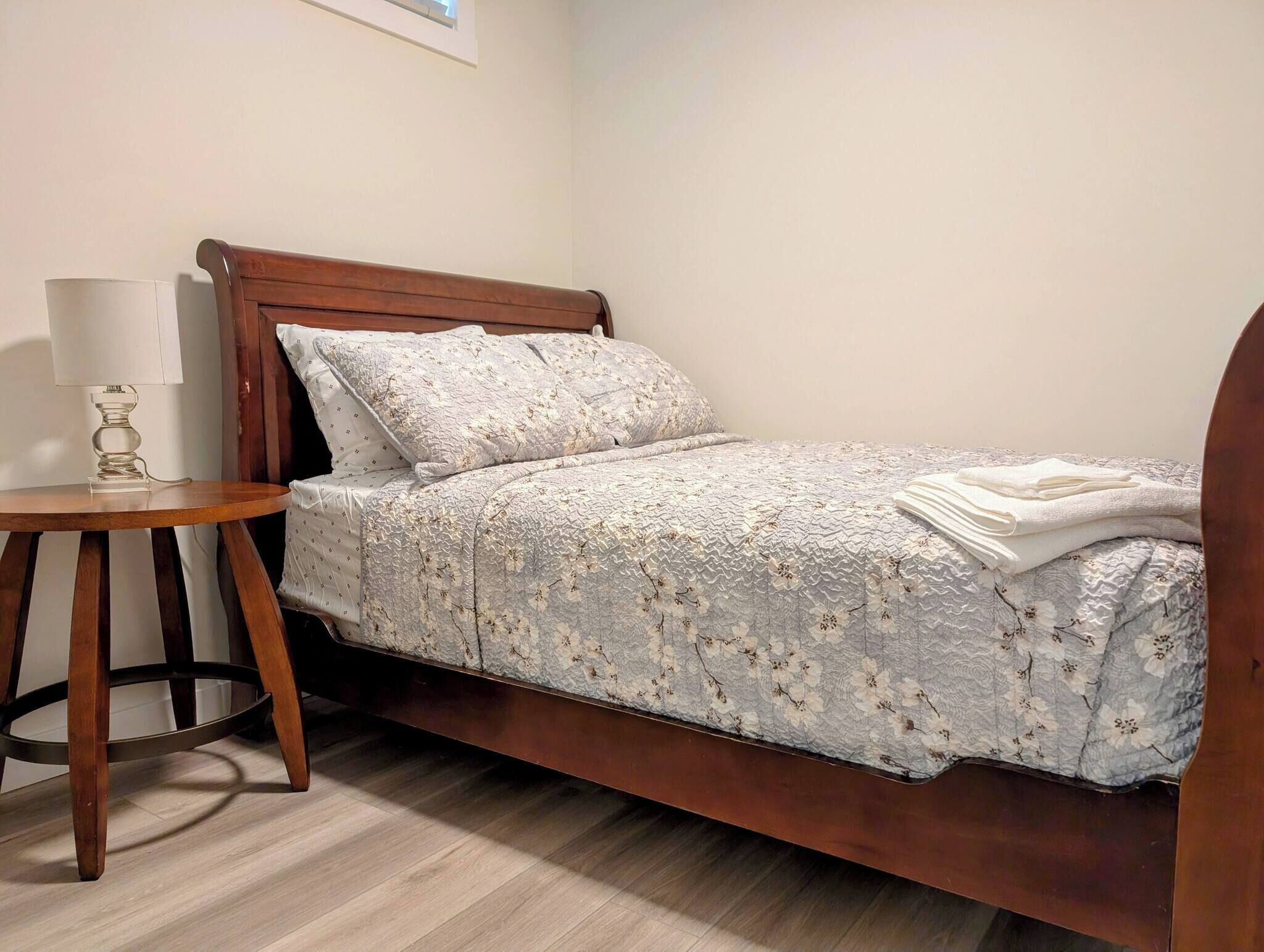 A single bed with a floral bedspread, a bedside table with a lamp, and a wooden floor.