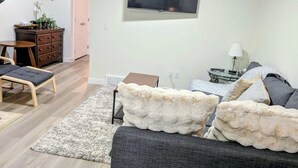 A modern living room with a grey sofa, a fluffy white throw, and a flat-screen TV mounted on the wall. - 2 Bedroom Guest Suite in SW (Calgary)