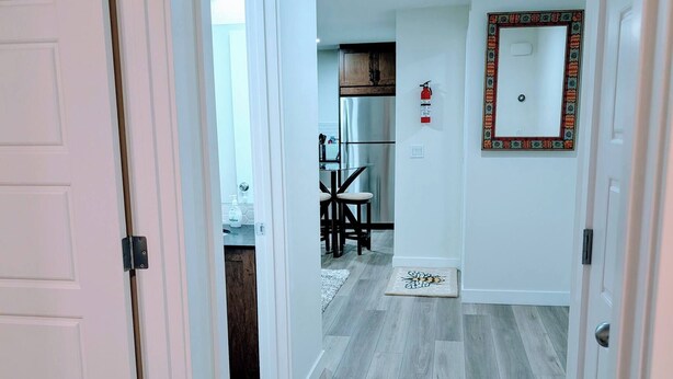 A hallway with a wooden floor, white walls, and a dining area with a table and chairs. - 2 Bedroom Guest Suite in SW (Calgary)